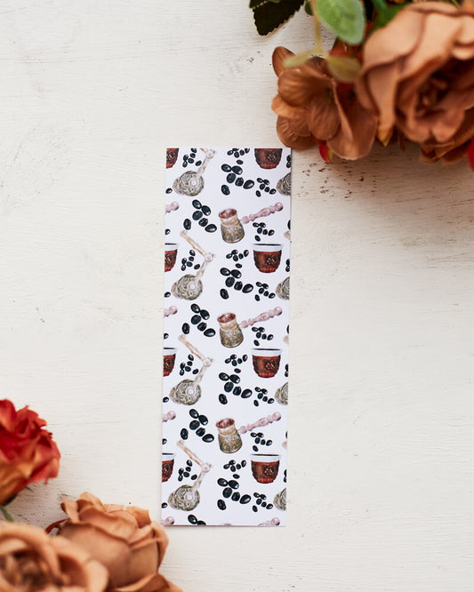 A glossy 2 X 6 inch bookmark depicting a pattern of coffee beans, cups of turkish coffee, a Turkish coffee grinder and a cezve.