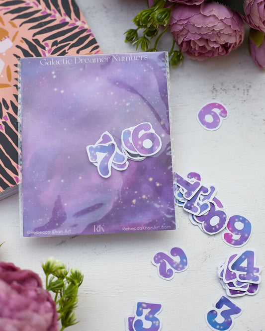 A sticker pack titled "Galactic Dreamer Numbers" with the stickers strewn on a table.  The stickers are starry galaxies in the shape of numbers.