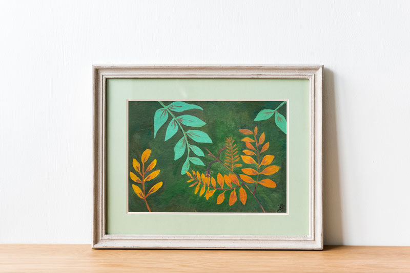 Art print of a gouache painting of gold and teal leaves reaching towards each other against a dark green background in a painted white frame with pale green matting.