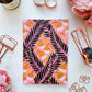 Flat Lay Photograph of Peach Poetry A5 Notebook Featuring Black Leaves on Intertwining Branches with Semi-Abstract Flowers in Light Brown on a Peach Pink Background Surrounded by Pink Flowers and Stationery Supplies.