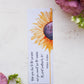 A glossy 2 x 6 inch bookmark depicting a yellow sunflower painted in watercolor with the lower petals dripping.  On the side is written, "Keep your face to the sunshine and you cannot see the shadow.  It's what sunflowers do. -Helen Keller."