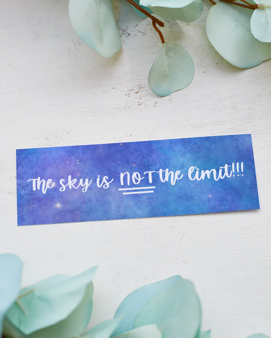 A glossy 2 x 6 bookmark depicting a starry galaxy against a light purple background with the words "The sky is NOT the limit!!!" in white hand lettering across the middle.