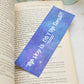A glossy 2 x 6 bookmark depicting a starry galaxy against a light purple background with the words "The sky is NOT the limit!!!" in white hand lettering across the middle on an open book with leaves in the background.