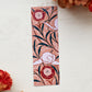 A glossy 2 x 6 inch bookmark depicting delicate branches, scrolling leaves, and semi-abstract flowers.