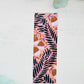 A glossy 2 x 6 bookmark depicting scrolling branches, abstract flowers, and a peachy pink background.
