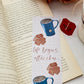 A glossy 2 X 6 bookmark with a pale yellow grid background depicting large mugs of tea and biscuits with the words "life begins after chai..." in script lettering across the middle on an open book next to a cup of tea with orange and brown flowers in the background.