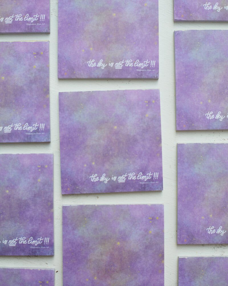 Multiple notepads depicting a starry galaxy against a light purple background with the words "The sky is NOT the limit!!!" in white hand lettering across the bottom.