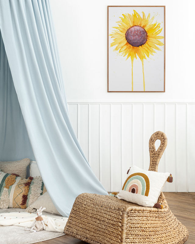 A child's room or nursery with a large watercolor painting of a sunflower with petals radiating outward and two petals dripping down to the bottom of the painting.