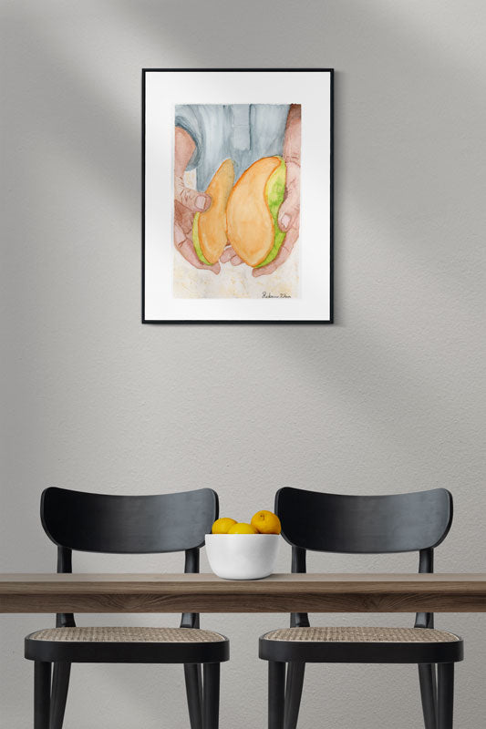 A dining room with an art print of a watercolor painting of two hands holding a bright mango that has been cut into to reveal the inside.