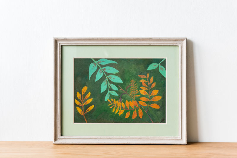 Art print of a gouache painting of gold and teal leaves reaching towards each other against a dark green background in a painted white frame with pale green matting.