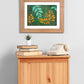 A small side table with books, a plant, a telephone, and above it, hanging on the wall in a wooden frame is an art print of a gouache painting of gold and teal leaves reaching towards each other against a dark green background.