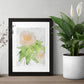 Framed art print of a peach rose painted with watercolors in a loose, impressionist style on a table in between two plants.