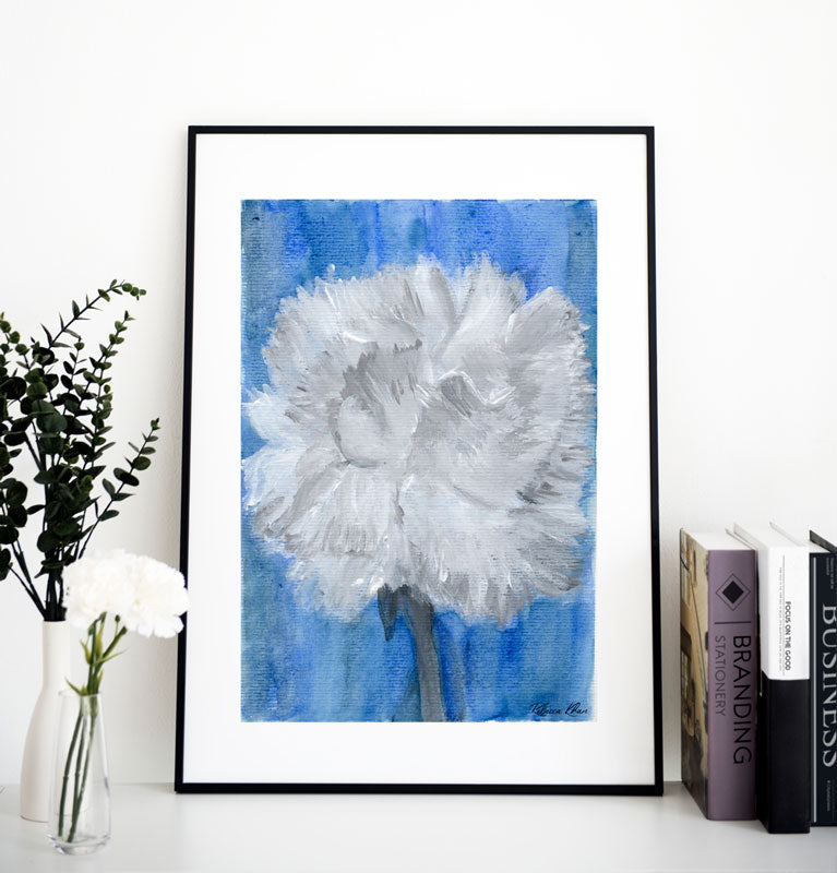 Art print of a mix media abstract floral painting of a white carnation on a blue background in a black frame on a shelf next to books and vases of flowers.